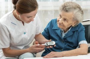 caregiver testing senior womans blood sugar